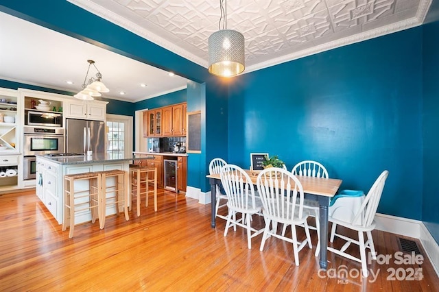 dining area with beverage cooler, light hardwood / wood-style floors, and crown molding