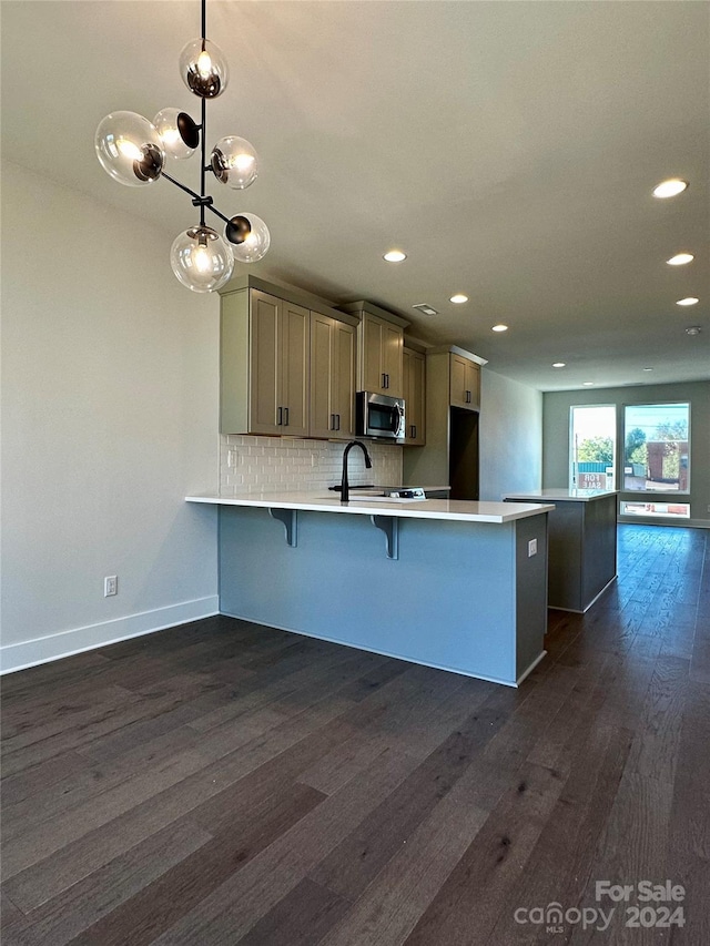 kitchen featuring kitchen peninsula, tasteful backsplash, a kitchen bar, dark hardwood / wood-style floors, and decorative light fixtures