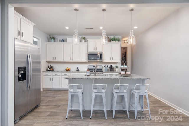 kitchen featuring white cabinets, hanging light fixtures, stainless steel appliances, and an island with sink