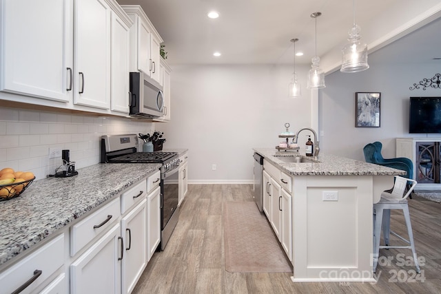 kitchen with a kitchen island with sink, stainless steel appliances, sink, white cabinets, and light hardwood / wood-style floors