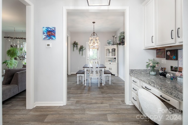 kitchen featuring light stone countertops, decorative light fixtures, dark wood-type flooring, a chandelier, and white cabinetry