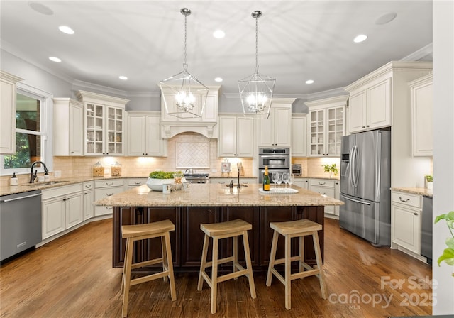 kitchen with sink, hanging light fixtures, a kitchen island with sink, stainless steel appliances, and light stone countertops