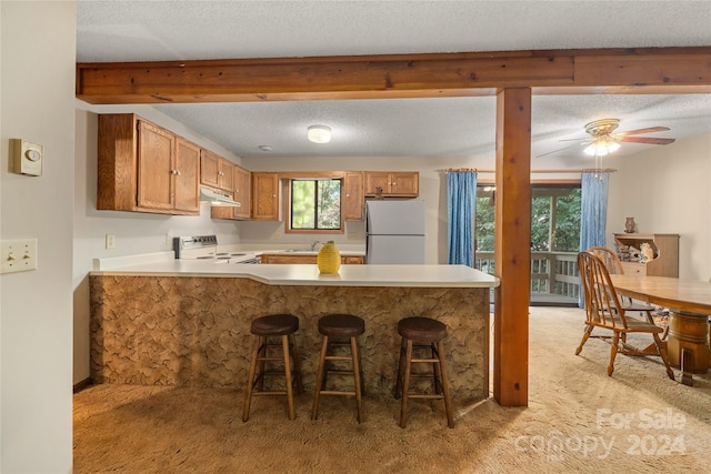 kitchen featuring white appliances, light colored carpet, kitchen peninsula, ceiling fan, and a textured ceiling