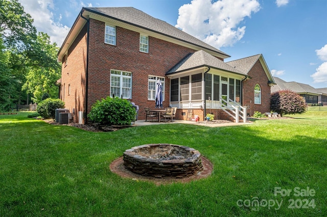 rear view of property featuring a fire pit, a yard, a sunroom, a patio, and central AC