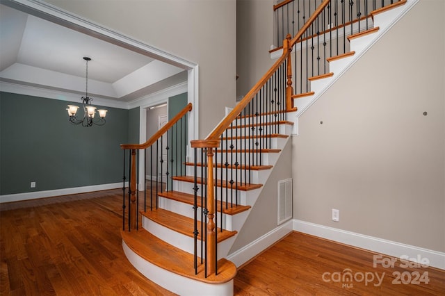 stairs featuring a notable chandelier, hardwood / wood-style flooring, a raised ceiling, and crown molding