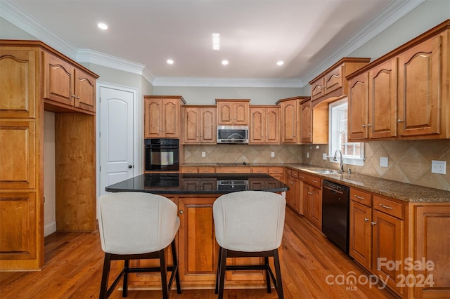 kitchen with a kitchen breakfast bar, hardwood / wood-style flooring, black appliances, sink, and a center island