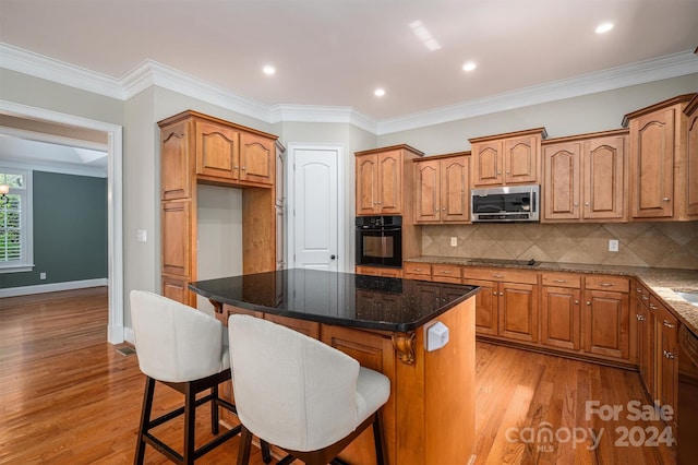 kitchen with dark stone countertops, ornamental molding, black appliances, a center island, and light wood-type flooring