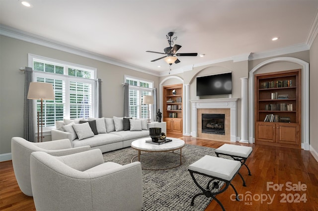 living room featuring crown molding, dark hardwood / wood-style floors, a tiled fireplace, and ceiling fan