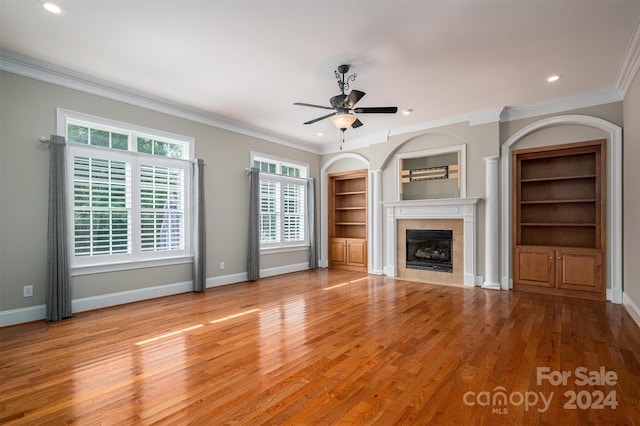 unfurnished living room with light hardwood / wood-style flooring, a tiled fireplace, ceiling fan, and crown molding