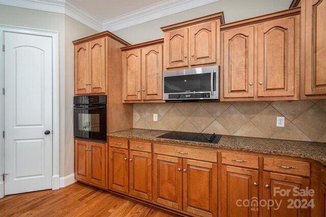 kitchen with tasteful backsplash, black appliances, light hardwood / wood-style floors, dark stone countertops, and crown molding