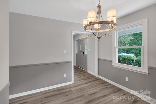 unfurnished dining area with wood-type flooring and a chandelier