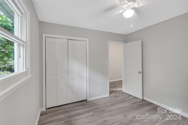 unfurnished bedroom with multiple windows, light hardwood / wood-style flooring, ceiling fan, and a closet