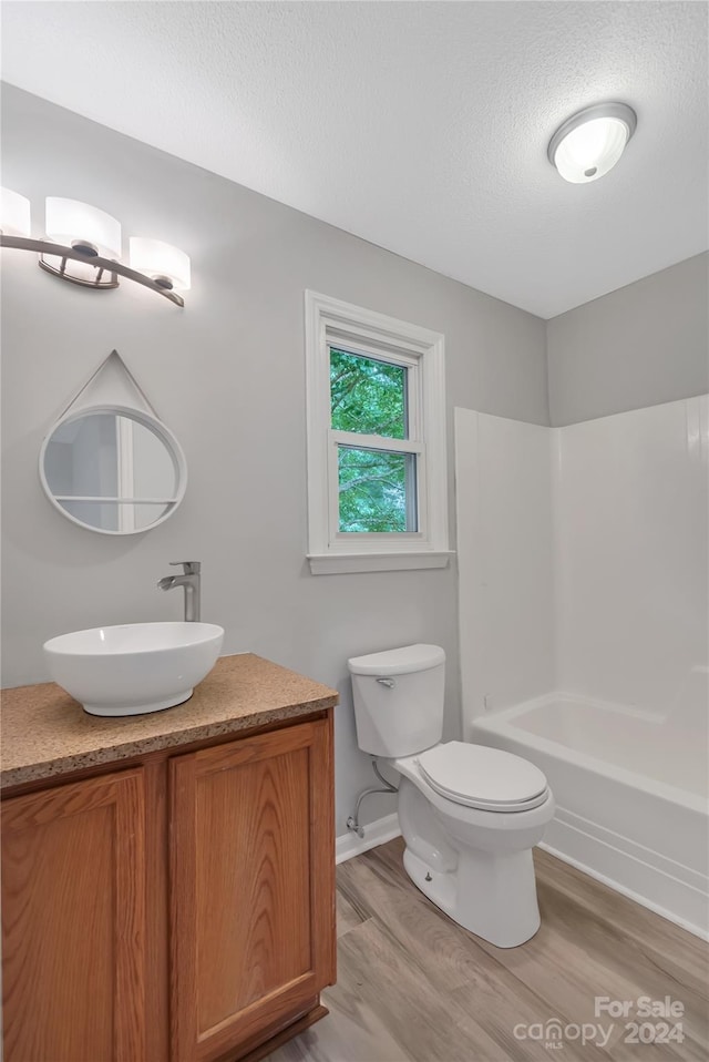 full bathroom featuring vanity, wood-type flooring, a textured ceiling, shower / washtub combination, and toilet