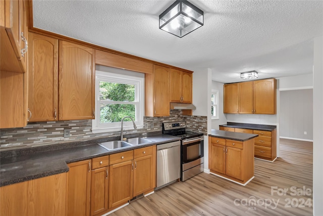 kitchen with appliances with stainless steel finishes, a textured ceiling, light hardwood / wood-style floors, and sink