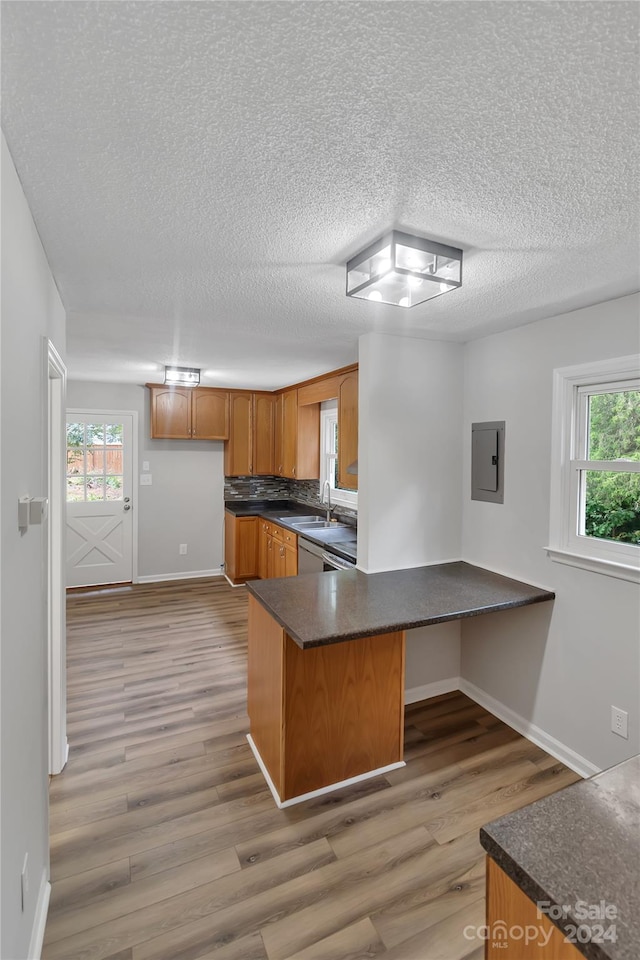 kitchen with electric panel, kitchen peninsula, tasteful backsplash, wood-type flooring, and a textured ceiling