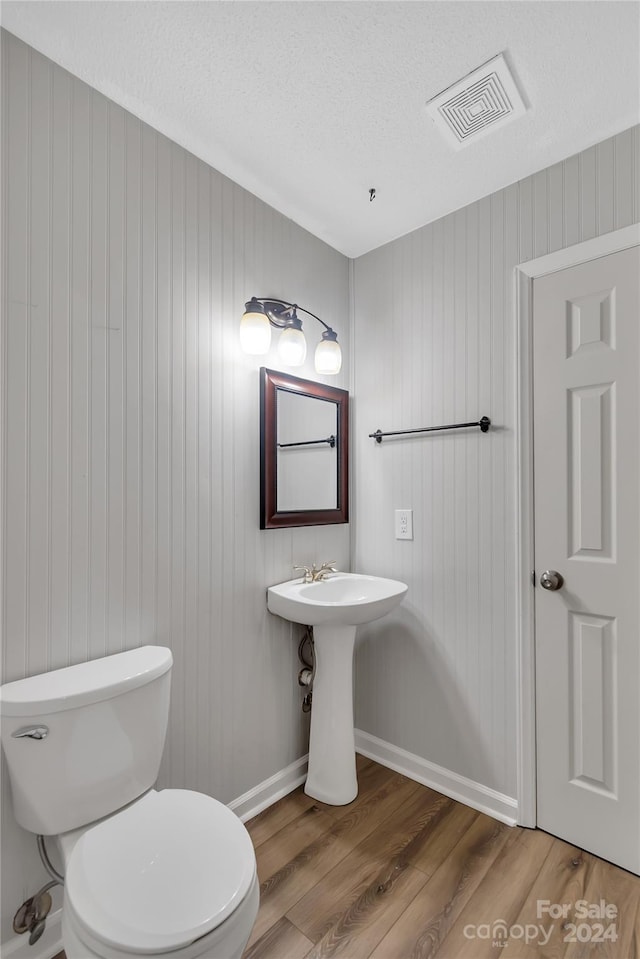 bathroom featuring toilet, wooden walls, hardwood / wood-style floors, and a textured ceiling