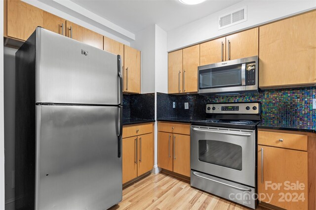 kitchen with appliances with stainless steel finishes, decorative backsplash, and light hardwood / wood-style floors