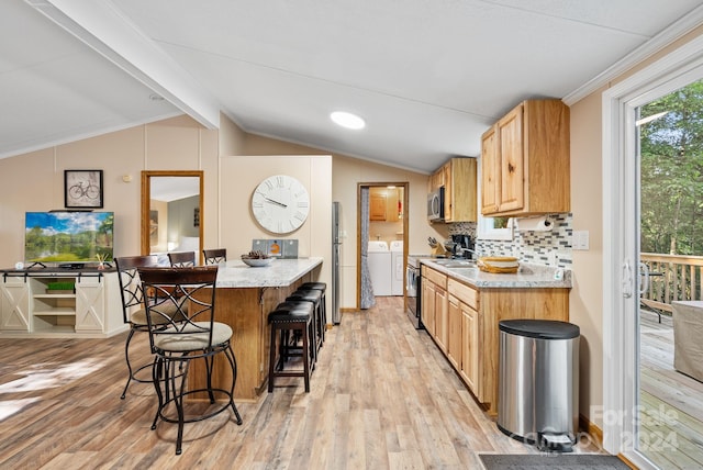 kitchen with appliances with stainless steel finishes, washing machine and clothes dryer, vaulted ceiling with beams, light hardwood / wood-style floors, and a breakfast bar area