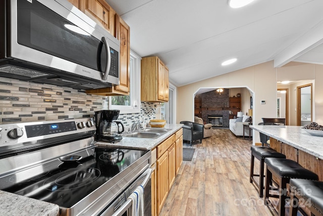 kitchen with appliances with stainless steel finishes, light wood-type flooring, tasteful backsplash, sink, and vaulted ceiling with beams