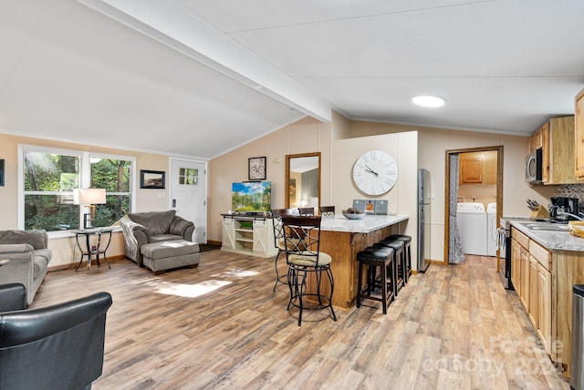 kitchen with a breakfast bar, vaulted ceiling with beams, washer and dryer, appliances with stainless steel finishes, and light hardwood / wood-style floors