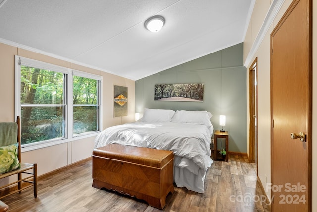 bedroom with a textured ceiling, light wood-type flooring, lofted ceiling, and crown molding