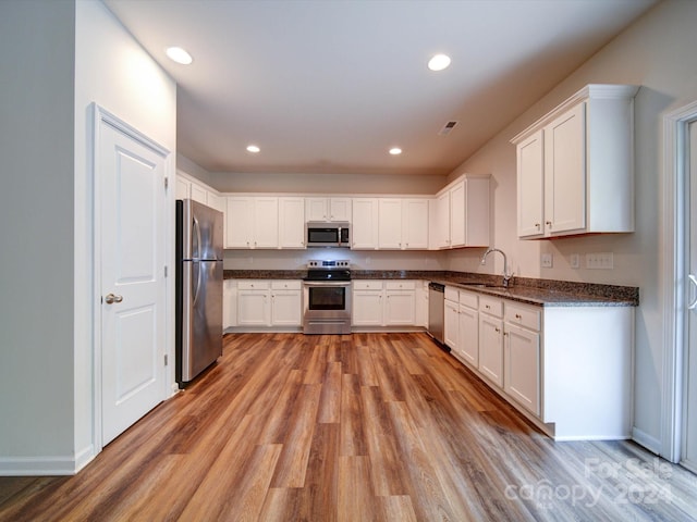 kitchen with light hardwood / wood-style flooring, sink, white cabinetry, appliances with stainless steel finishes, and dark stone countertops