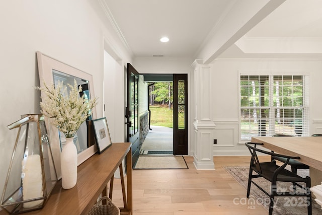 foyer with visible vents, light wood finished floors, ornate columns, crown molding, and a decorative wall