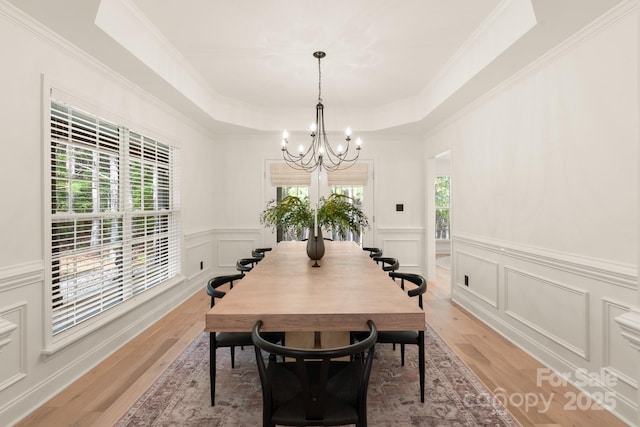 dining room featuring an inviting chandelier, a tray ceiling, light wood-style flooring, and plenty of natural light