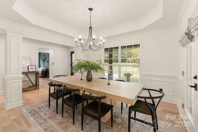 dining area featuring an inviting chandelier, a tray ceiling, light wood-style flooring, and a decorative wall