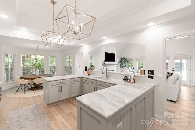 kitchen with light wood finished floors, plenty of natural light, an inviting chandelier, and a sink