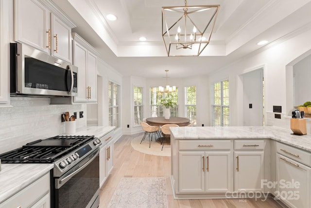 kitchen with a notable chandelier, appliances with stainless steel finishes, white cabinets, crown molding, and a raised ceiling