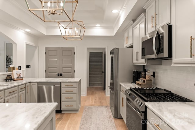 kitchen with a raised ceiling, an inviting chandelier, appliances with stainless steel finishes, and ornamental molding