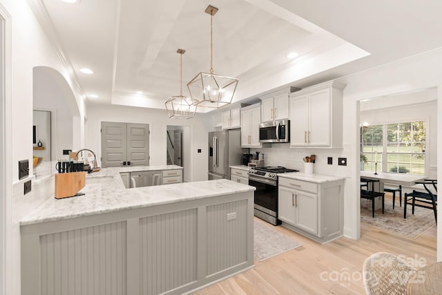 kitchen featuring a notable chandelier, stainless steel appliances, light wood finished floors, decorative backsplash, and a raised ceiling