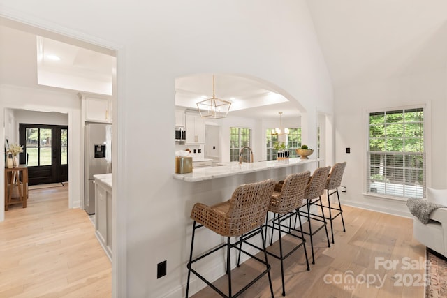 kitchen with arched walkways, stainless steel appliances, white cabinets, a kitchen bar, and light wood-type flooring