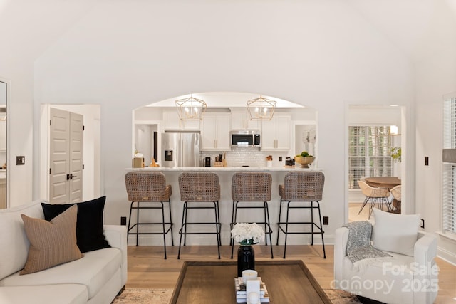 living area featuring light wood-style floors, arched walkways, and high vaulted ceiling