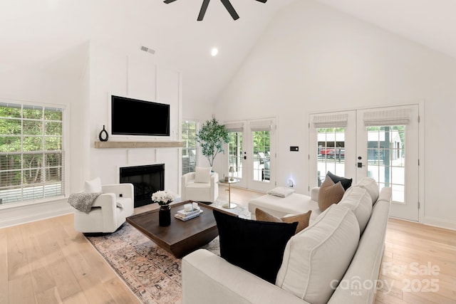 living area with visible vents, a ceiling fan, french doors, a fireplace, and light wood finished floors