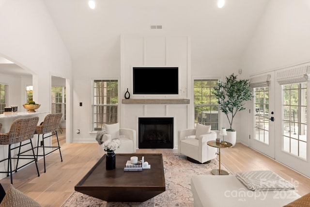 living room with high vaulted ceiling, french doors, a fireplace, and light wood-type flooring