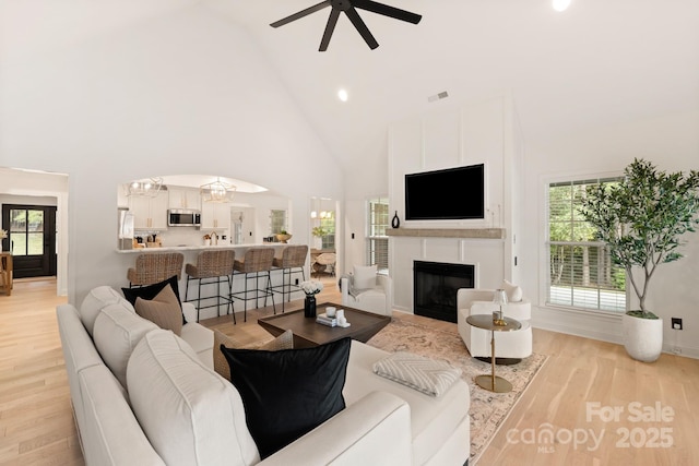 living area featuring ceiling fan with notable chandelier, plenty of natural light, light wood-style floors, and visible vents