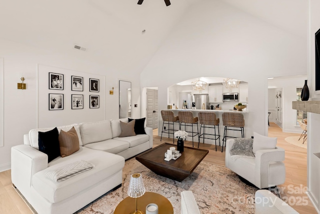 living room with light wood-type flooring, visible vents, high vaulted ceiling, a ceiling fan, and arched walkways