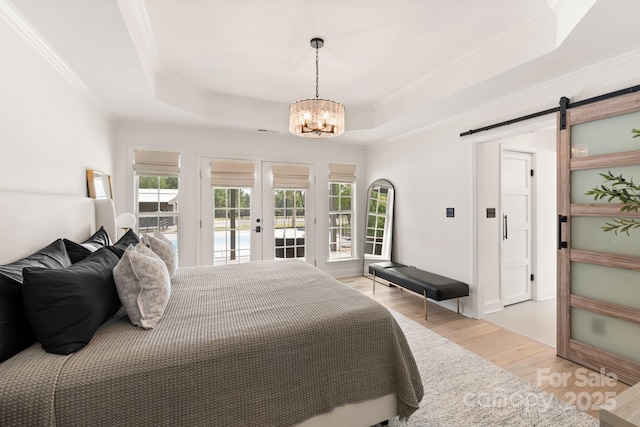 bedroom featuring a tray ceiling, a barn door, french doors, light wood-style floors, and access to exterior