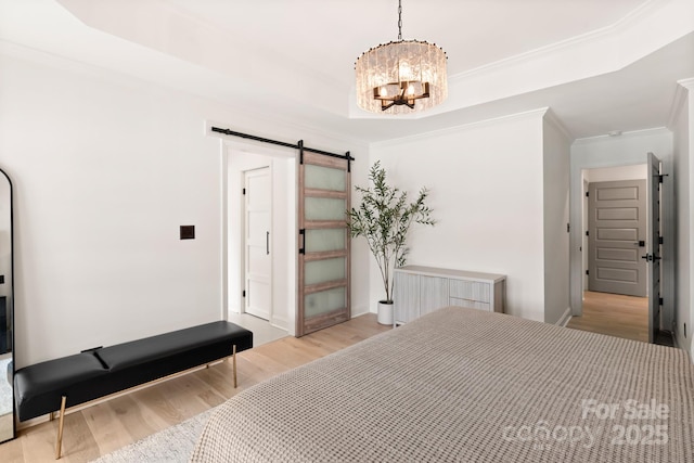 bedroom with light wood-style floors, an inviting chandelier, a raised ceiling, and a barn door