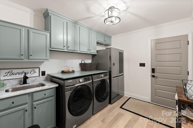 clothes washing area featuring cabinet space, ornamental molding, a sink, light wood-style floors, and independent washer and dryer