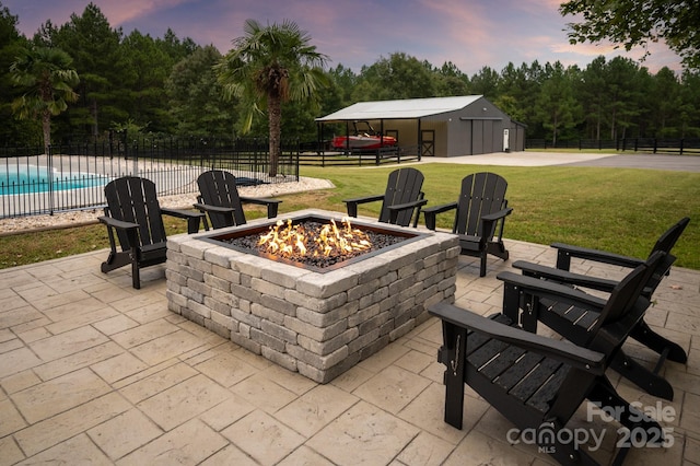 patio terrace at dusk featuring fence, a fenced in pool, a fire pit, a garage, and a lawn