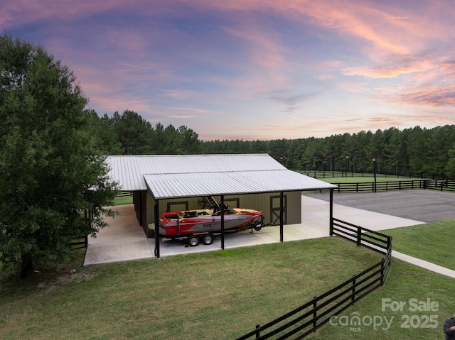 view of car parking with an exterior structure, a carport, and a wooded view