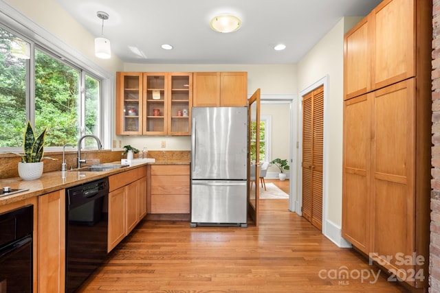 kitchen featuring black appliances, light hardwood / wood-style flooring, hanging light fixtures, sink, and light stone counters