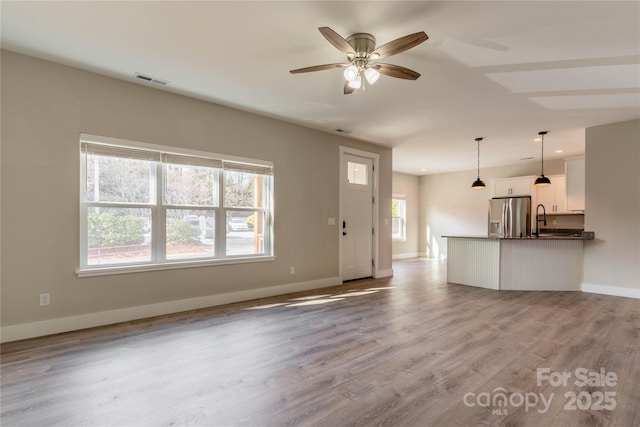 unfurnished living room with ceiling fan, sink, light hardwood / wood-style flooring, and a wealth of natural light