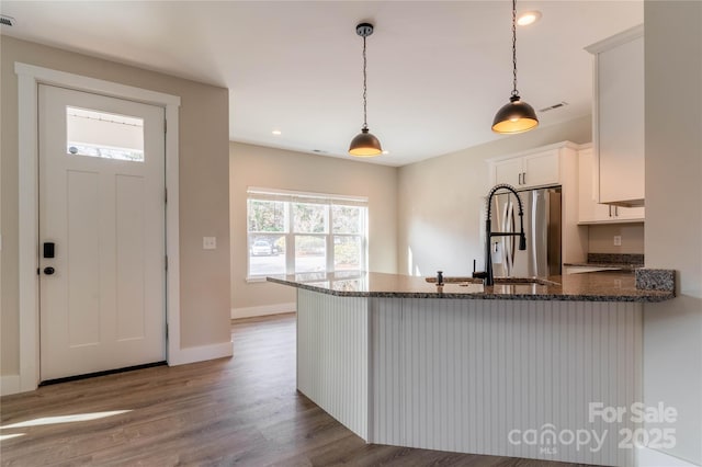 kitchen featuring decorative light fixtures, sink, white cabinets, stainless steel refrigerator with ice dispenser, and light hardwood / wood-style flooring