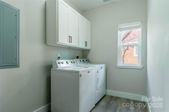 clothes washing area with hardwood / wood-style flooring, cabinets, electric panel, and washing machine and clothes dryer