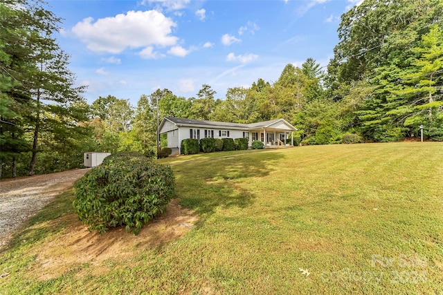 ranch-style home featuring a storage unit, covered porch, and a front yard