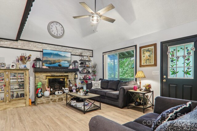 living room featuring a textured ceiling, a stone fireplace, wood-type flooring, lofted ceiling, and ceiling fan